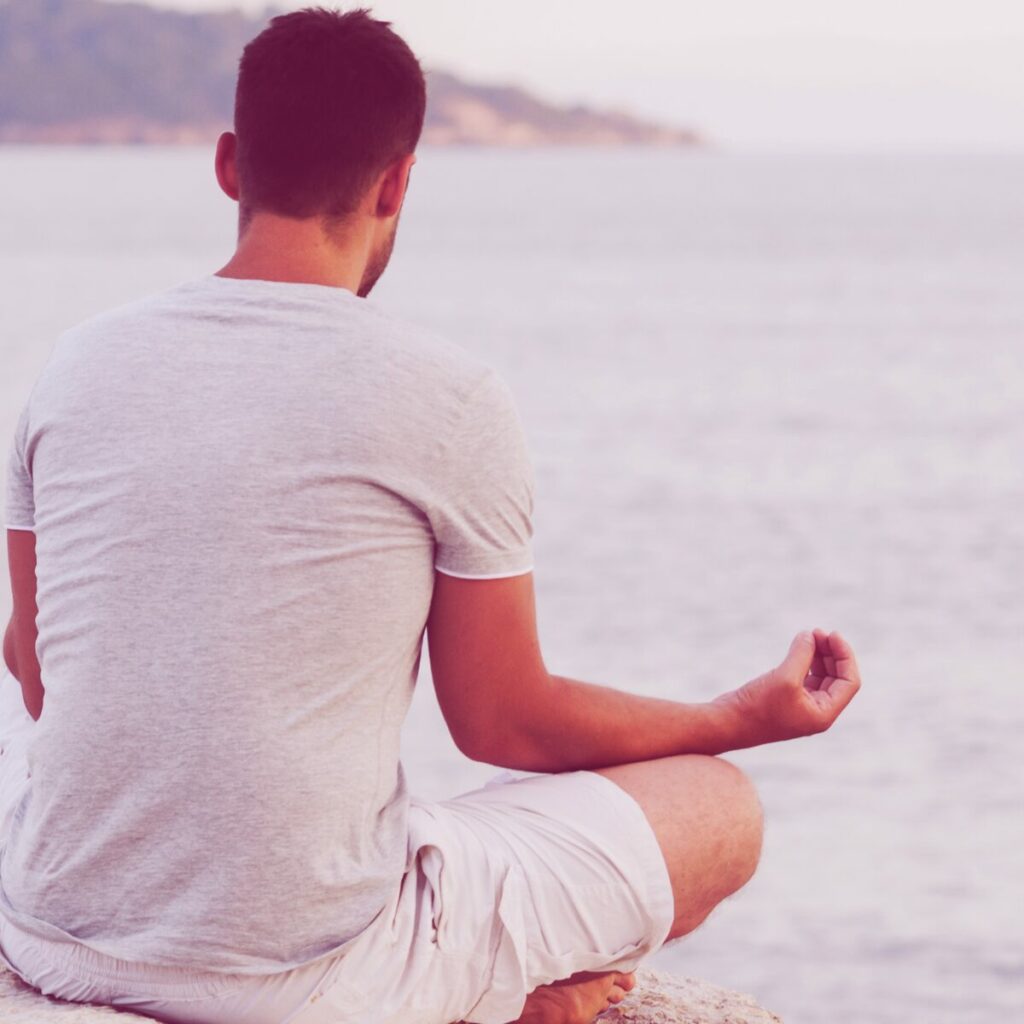 Un uomo su una spiaggia che fa meditazione.