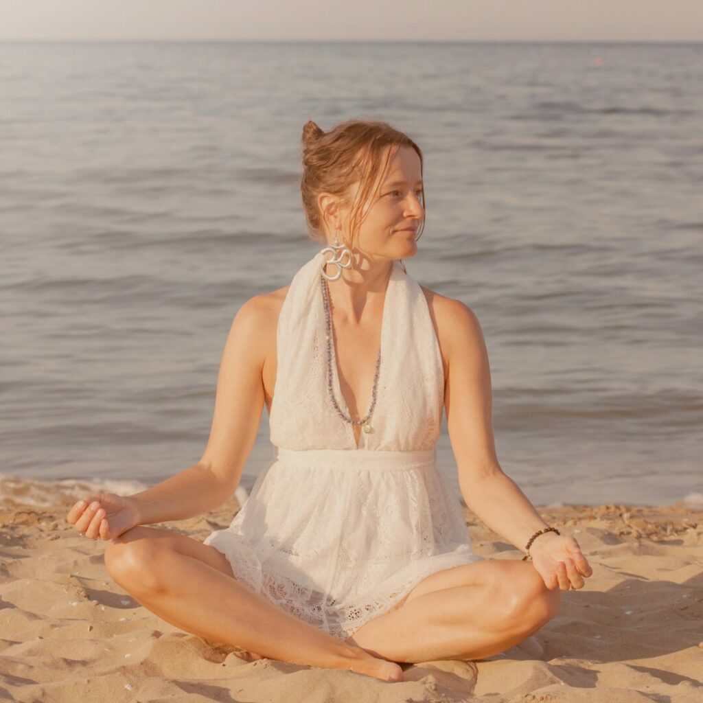 Una ragazza sulla spiaggia a gambe incrociate che mostra come meditare.